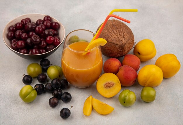 Vista superior de cerezas rojas en un tazón con jugo de durazno fresco con frutas frescas como melocotones ciruelas cerezas verdes aisladas sobre fondo blanco