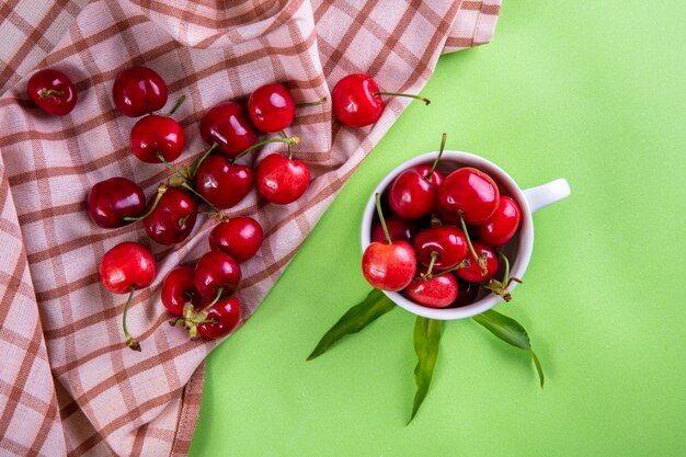 Vista superior de cerezas en una taza con una toalla de cocina en verde claro