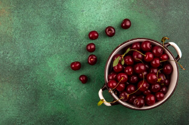 Vista superior de las cerezas en un tazón y sobre fondo verde con espacio de copia