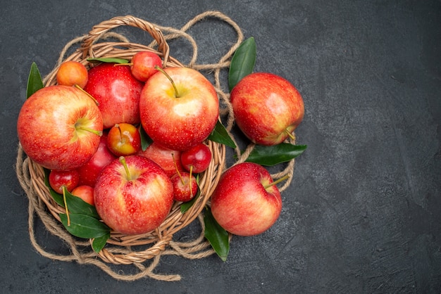 Vista superior de la cesta de frutas de las apetecibles manzanas y cerezas con hojas