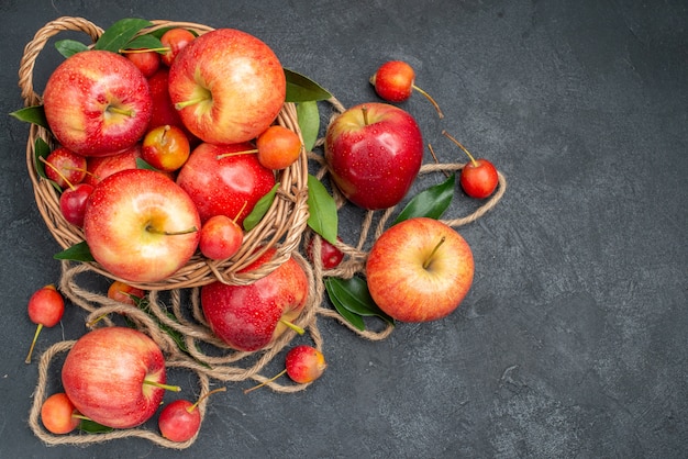 Vista superior de la cesta de frutas con frutas manzanas cerezas con cuerda de hojas
