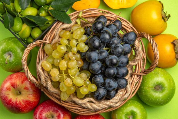 Vista superior de la cesta de frutas de uvas verdes y negras caquis manzanas cítricos