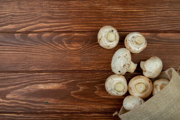 Vista superior de champiñones frescos esparcidos de un saco en superficie de madera rústica con espacio de copia