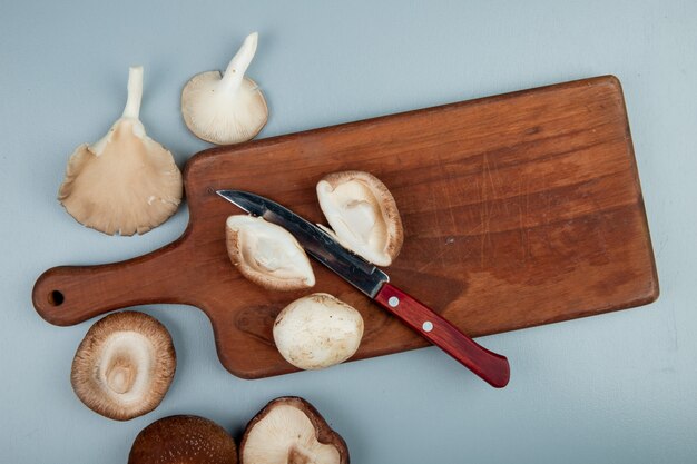 Vista superior de champiñones frescos en una tabla para cortar madera con cuchillo de cocina en azul claro