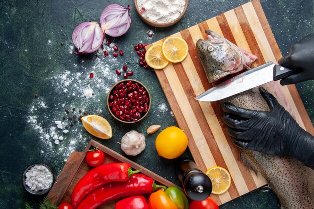 Vista superior del chef cortando la cabeza de pescado en la tabla de cortar, molinillo de pimienta, tazón de harina, semillas de granada en un tazón en la mesa de la cocina