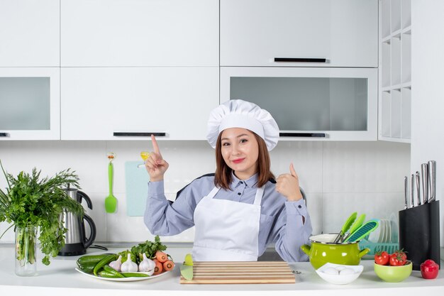 Vista superior de la chef mujer sorprendida y verduras frescas apuntando hacia arriba haciendo gesto de ok en la cocina blanca