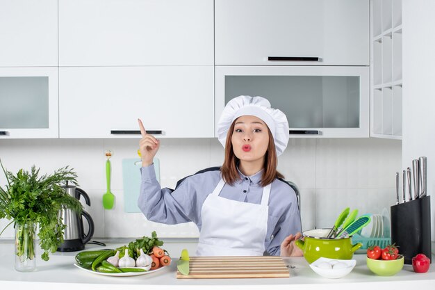 Vista superior de la chef mujer sorprendida y verduras frescas apuntando hacia el lado derecho en la cocina blanca