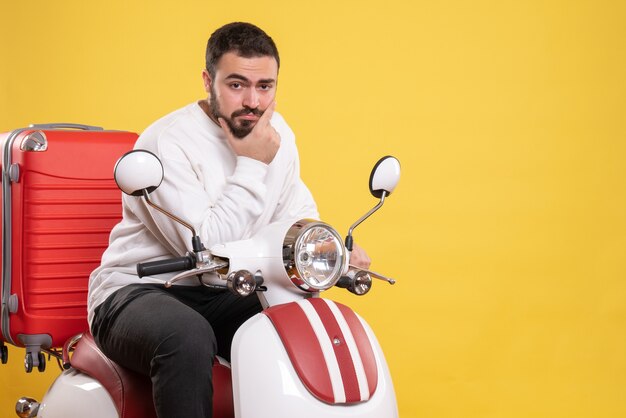 Vista superior del chico joven confiado que se sienta en la motocicleta con la maleta sobre fondo amarillo aislado