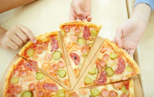 Vista superior de chicos cogiendo una porción de pizza