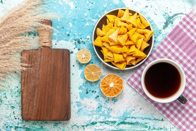 Vista superior de chips de galleta con taza de té en la superficie azul