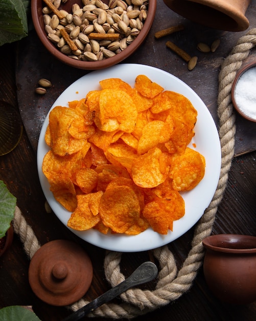 Una vista superior de chips de naranja calientes dentro de la placa blanca con maní en el escritorio de madera, chips de aperitivos, sal de especias