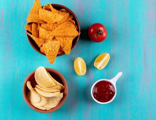 Vista superior chips en un tazón con tomate limón y salsa en horizontal azul