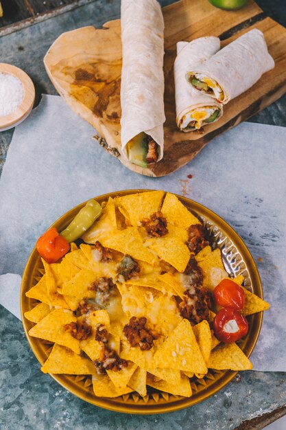 Vista superior de chips de tortilla mexicana de nachos en placa con tacos mexicanos en tabla de cortar