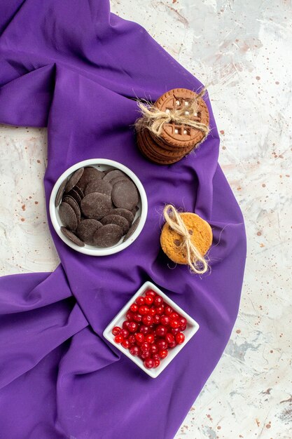 Vista superior de chocolate y bayas en tazones galletas de mantón morado atadas con una cuerda