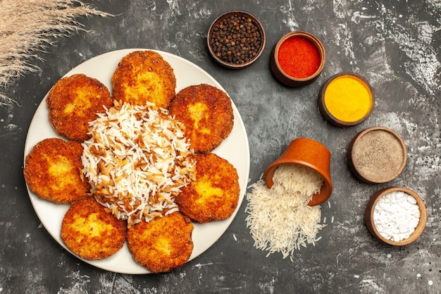 Vista superior de chuletas fritas con arroz cocido y condimentos en un plato de carne de superficie oscura