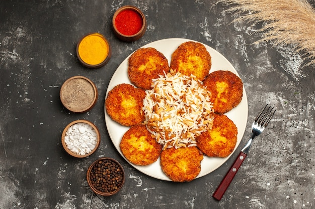 Vista superior de chuletas fritas con arroz cocido y condimentos en un plato de comida de superficie oscura foto carne