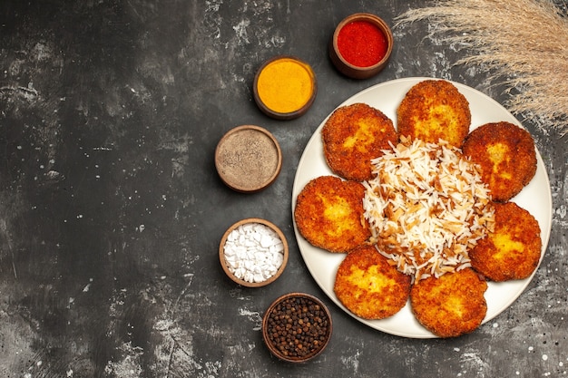 Foto gratuita vista superior de chuletas fritas con arroz cocido y condimentos en un plato de superficie oscura.