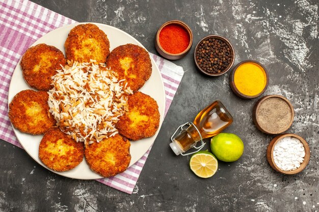 Vista superior de chuletas fritas con arroz cocido y condimentos en rissole de carne de superficie oscura