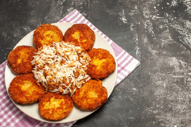 Vista superior de chuletas fritas con arroz cocido en un escritorio oscuro plato de comida de carne rissole