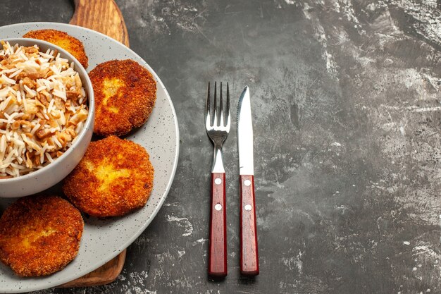 Vista superior de chuletas fritas con arroz cocido en un plato de escritorio oscuro rissole de carne