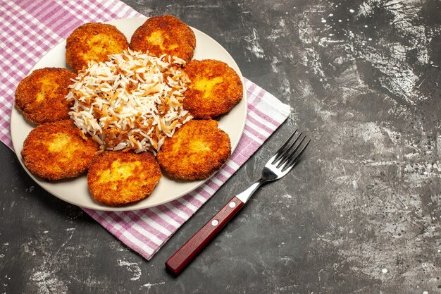 Vista superior chuletas fritas con arroz cocido en plato de rissole de carne de piso oscuro