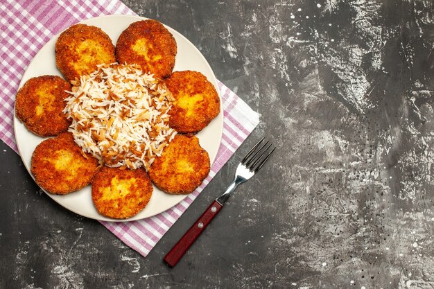 Vista superior chuletas fritas con arroz cocido en el plato de rissole de carne de superficie oscura