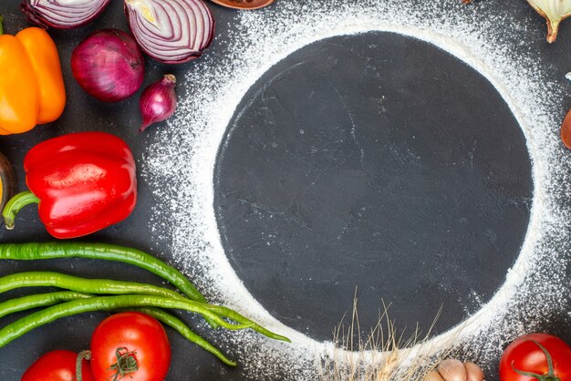 Vista superior círculo de harina espolvoreada tomates cebollas rojas pimientos verdes pimientos picantes en el espacio libre de la mesa