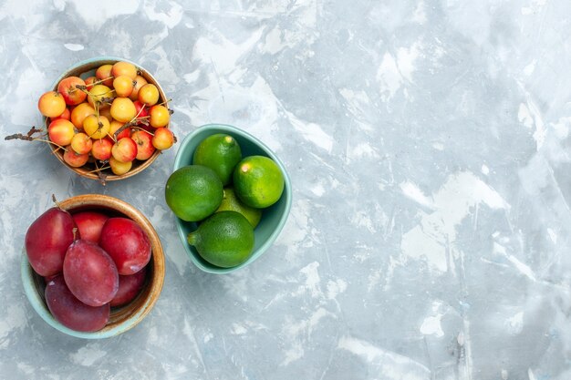 Vista superior de ciruelas y limones con cerezas dulces sobre superficie blanca clara