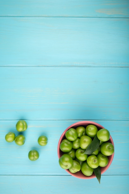 Foto gratuita vista superior de ciruelas verdes agrias en un recipiente en la mesa azul con espacio de copia