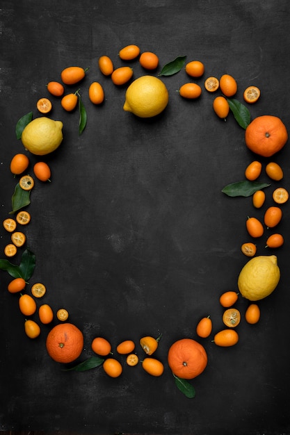 Vista superior de cítricos como kumquats, limones y mandarinas en forma circular sobre superficie negra