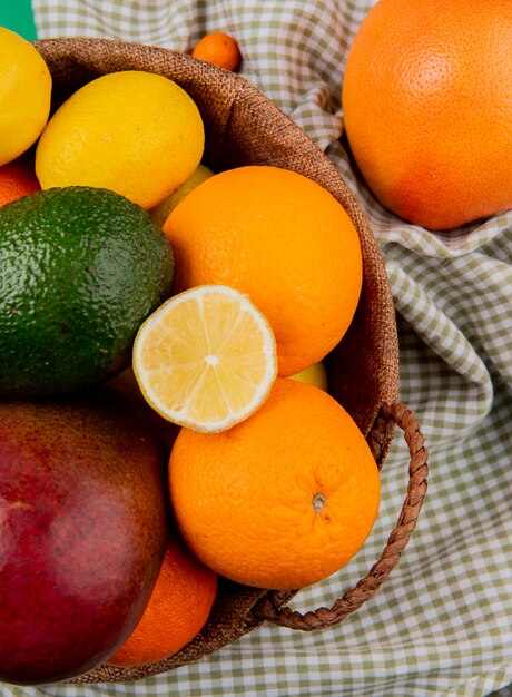 Vista superior de cítricos como mango naranja aguacate limón en canasta sobre fondo de tela escocesa