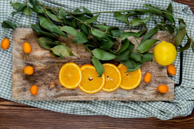 Foto gratuita vista superior de cítricos como naranja kumquat de limón con hojas en la tabla de cortar sobre tela y fondo de madera