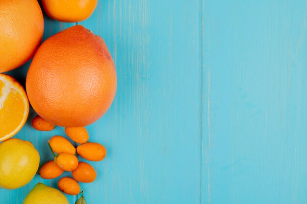 Vista superior de cítricos como naranja mandarina limón y kumquats en el lado izquierdo y fondo azul con espacio de copia