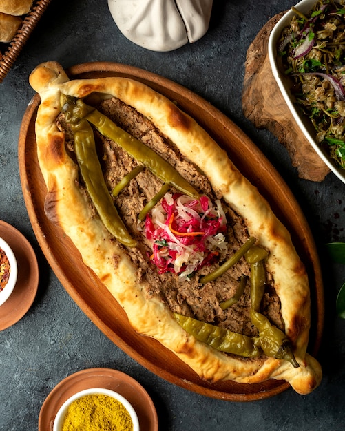 Vista superior de la cocina georgiana tradicional khachapuri con carne y pimiento verde picante en escabeche en una bandeja de madera