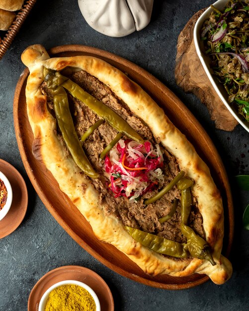 Vista superior de la cocina georgiana tradicional khachapuri con carne y pimiento verde picante en escabeche en una bandeja de madera