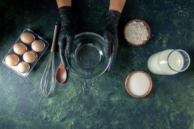 Vista superior cocinera preparándose para cocinar algo con leche, huevos y harina sobre una superficie oscura