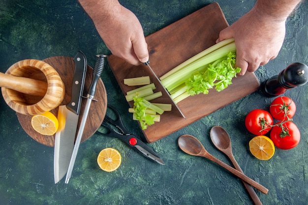 Vista superior cocinero masculino cortando el apio en la mesa oscura ensalada dieta comida fotografía en color salud alimentaria