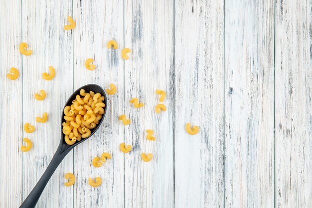 Foto gratuita vista superior codo macarrones pasta con cuchara a la izquierda con espacio de copia sobre fondo blanco de madera