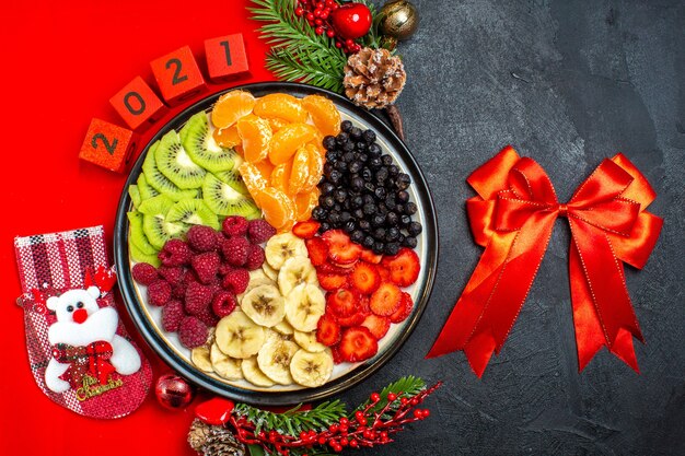 Vista superior de la colección de frutas frescas en accesorios de decoración de plato de cena ramas de abeto y números en una servilleta roja y cinta roja