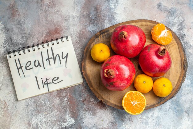 Vista superior de la colección de frutas frescas con granadas, naranjas y mandarinas en una bandeja de madera y un cuaderno con escritura de vida saludable sobre fondo de hielo