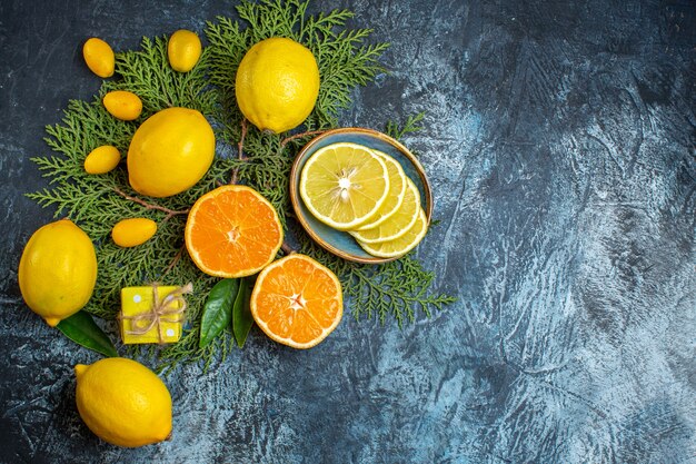 Vista superior de la colección de mitad y frutas cítricas enteras en ramas de abeto en el lado derecho sobre fondo oscuro