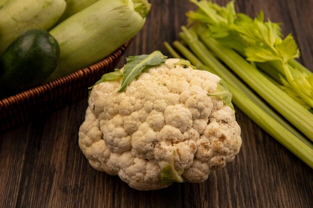 Vista superior de coliflor fresca con verduras como calabacines y pepinos en un balde sobre una superficie de madera