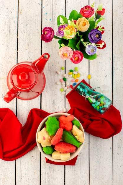 Foto gratuita vista superior de coloridas deliciosas galletas diferentes formadas dentro de la placa con caldera roja dulces y flores