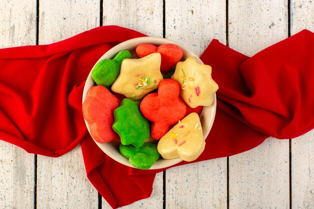 Vista superior de coloridas deliciosas galletas diferentes formadas dentro de un plato redondo con tejido rojo