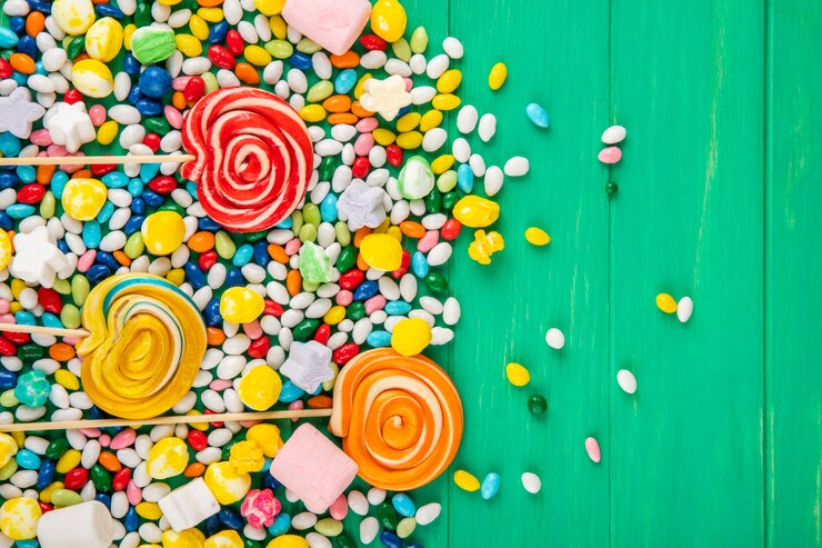 Foto gratuito vista superior de coloridos chupetines y caramelos en esmalte multicolor dispersos sobre fondo verde con espacio de copia