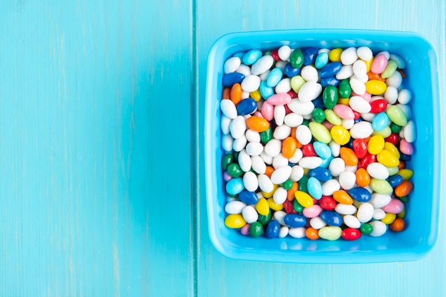 Vista superior de coloridos dulces de azúcar dulce en un recipiente sobre fondo de madera azul con espacio de copia