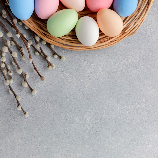 Vista superior de coloridos huevos de pascua en canasta con flores y espacio de copia