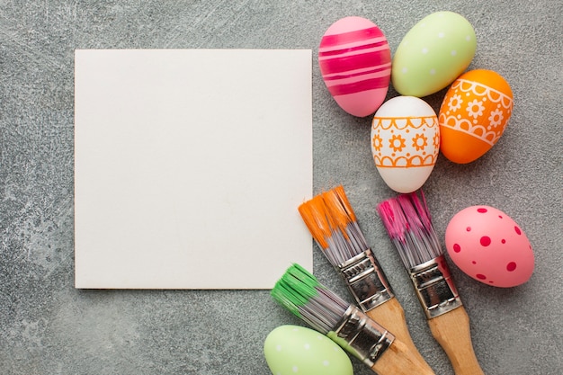 Vista superior de coloridos huevos de pascua con pinceles y papel