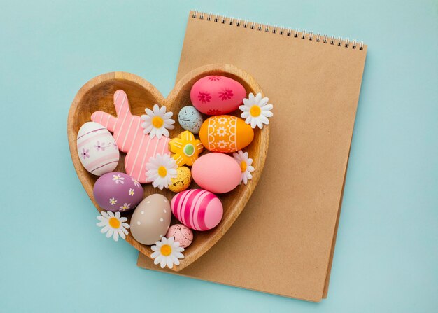 Vista superior de coloridos huevos de Pascua en placa en forma de corazón con cuaderno