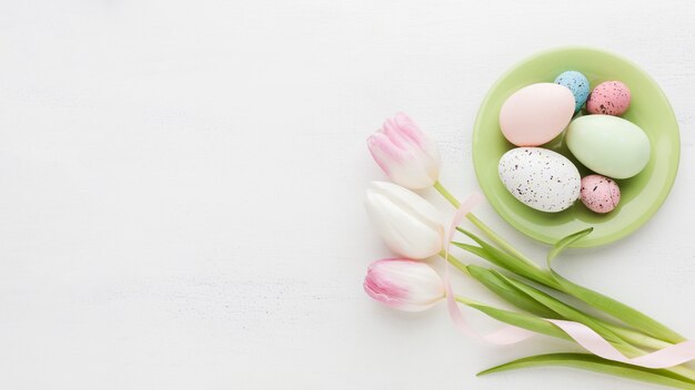 Vista superior de coloridos huevos de pascua en plato con tulipanes